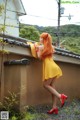 A woman in a yellow dress and red shoes leaning against a wall.