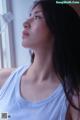 A woman in a white tank top looking out a window.
