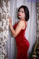 A woman in a red dress leaning against a curtain.