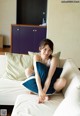 A woman sitting on a white couch with a blue pillow.