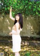 A woman in a white dress standing under a tree.