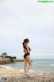 A woman in a black bathing suit standing on a rock by the ocean.