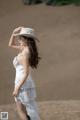 A woman in a white dress and hat standing in the sand.