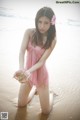 A woman in a pink dress sitting on the beach.