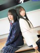 A couple of young women sitting on top of a desk.