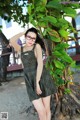 A woman wearing glasses standing next to a tree.