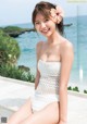 A woman in a white bathing suit sitting on a ledge by the ocean.