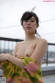 A naked asian woman standing on a balcony with a towel around her neck.