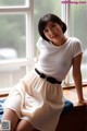 A woman sitting on a window sill wearing a white shirt and skirt.